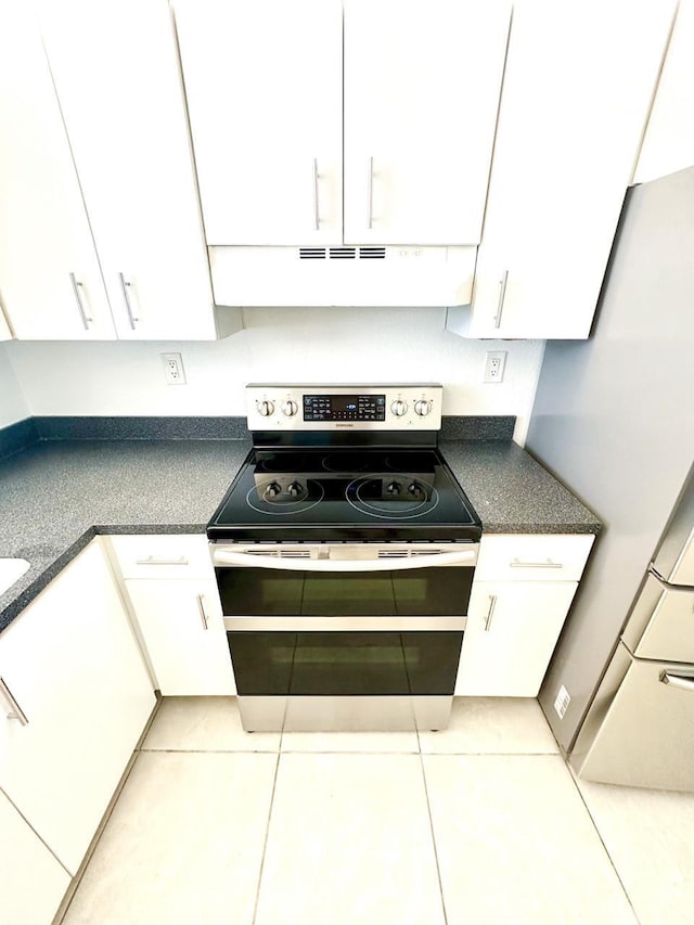 9235 SW 8th St Unit 402, Boca Raton, FL 33428 - kitchen with stainless steel range with electric stovetop, exhaust hood, white cabinetry, dark countertops, and light tile patterned flooring