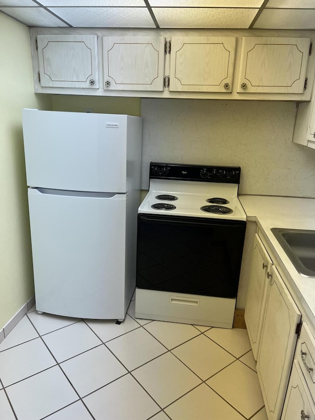 kitchen with freestanding refrigerator, a drop ceiling, range with electric cooktop, light tile patterned flooring, and light countertops