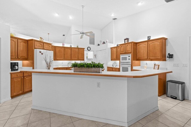 kitchen with white appliances, high vaulted ceiling, a spacious island, brown cabinets, and light tile patterned floors
