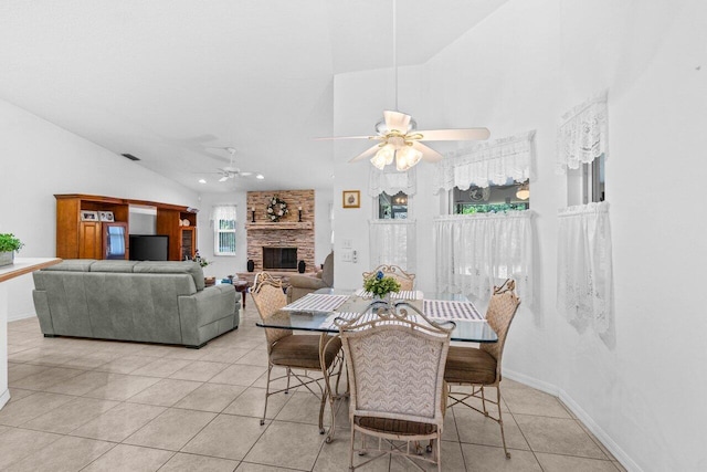 dining area featuring ceiling fan, light tile patterned floors, high vaulted ceiling, a stone fireplace, and baseboards