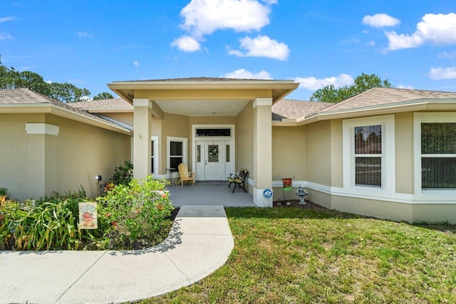 doorway to property featuring stucco siding, a lawn, and a shingled roof