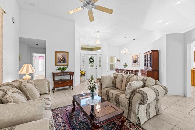 living room with light tile patterned floors, a ceiling fan, a chandelier, and high vaulted ceiling