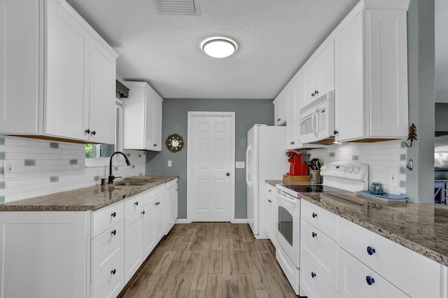 kitchen featuring white appliances, a sink, white cabinetry, decorative backsplash, and stone counters