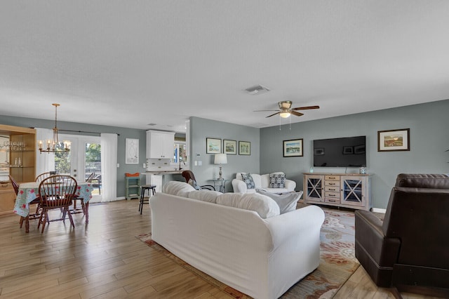 living room featuring a chandelier, a ceiling fan, light wood-type flooring, and baseboards