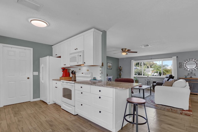 kitchen with white appliances, open floor plan, light wood finished floors, ceiling fan, and white cabinetry
