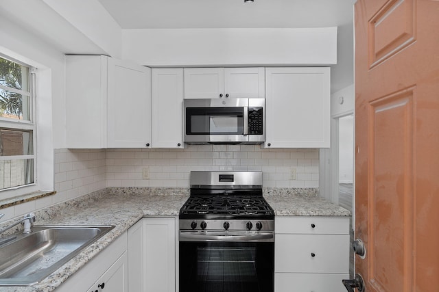 kitchen featuring stainless steel appliances, a sink, white cabinetry, and decorative backsplash