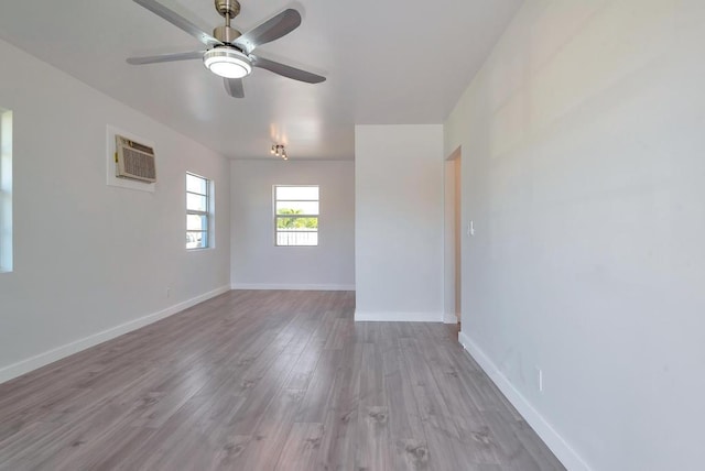 empty room featuring an AC wall unit, ceiling fan, wood finished floors, and baseboards