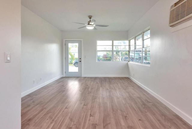 unfurnished room with a wall mounted air conditioner, a ceiling fan, baseboards, and light wood-type flooring