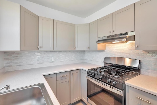 kitchen with gas stove, under cabinet range hood, gray cabinetry, a sink, and light countertops