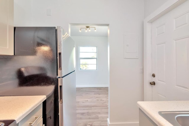 kitchen with freestanding refrigerator, light wood-type flooring, baseboards, light stone countertops, and electric panel