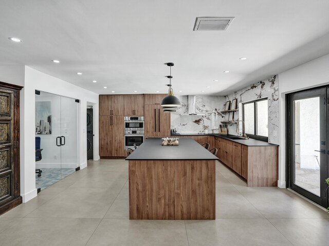 2708 NW 26th Cir, Boca Raton, FL 33431 - kitchen featuring stacked washer / dryer, double oven, a kitchen island, wall chimney exhaust hood, and modern cabinets