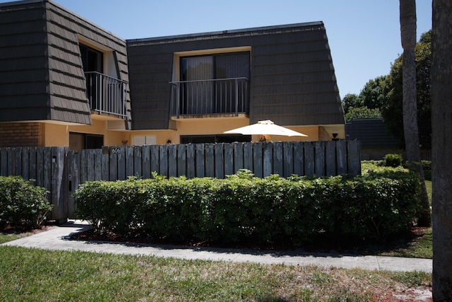 view of side of home featuring mansard roof, stucco siding, and fence
