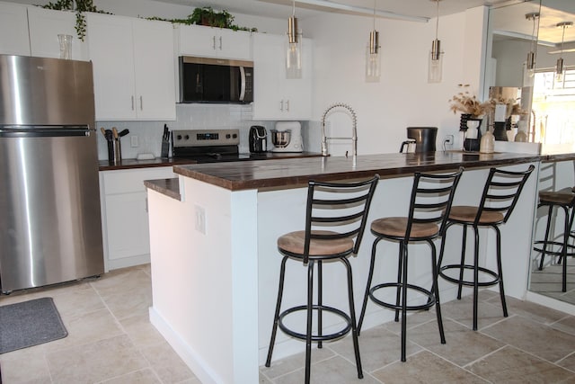 606 6th Way, West Palm Beach, FL 33407 - kitchen with stainless steel appliances, wooden counters, decorative backsplash, a kitchen bar, and white cabinetry