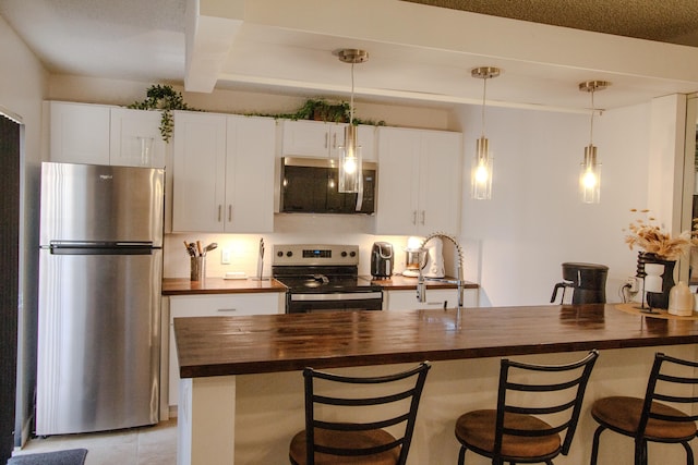 606 6th Way, West Palm Beach, FL 33407 - kitchen with butcher block counters, stainless steel appliances, a kitchen breakfast bar, hanging light fixtures, and white cabinetry