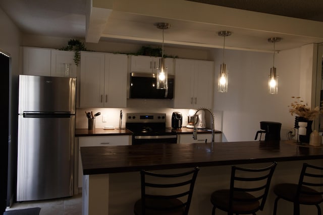 kitchen featuring a peninsula, stainless steel appliances, a breakfast bar, pendant lighting, and white cabinetry