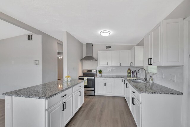 kitchen with stainless steel electric stove, wall chimney exhaust hood, a sink, light wood-style flooring, and backsplash