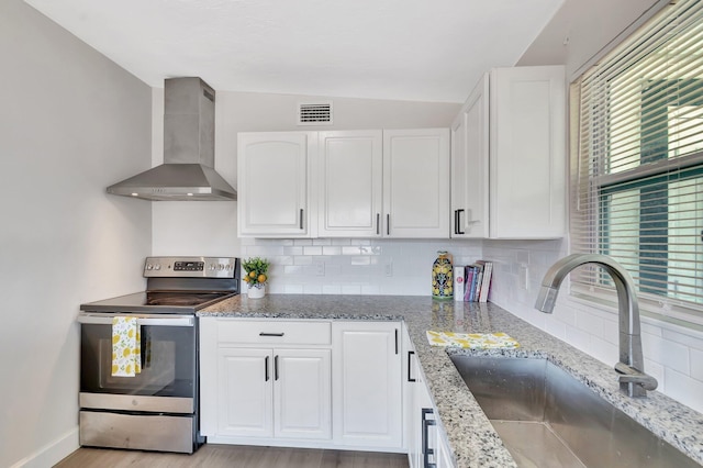 kitchen featuring stainless steel electric range, wall chimney exhaust hood, a sink, vaulted ceiling, and white cabinetry