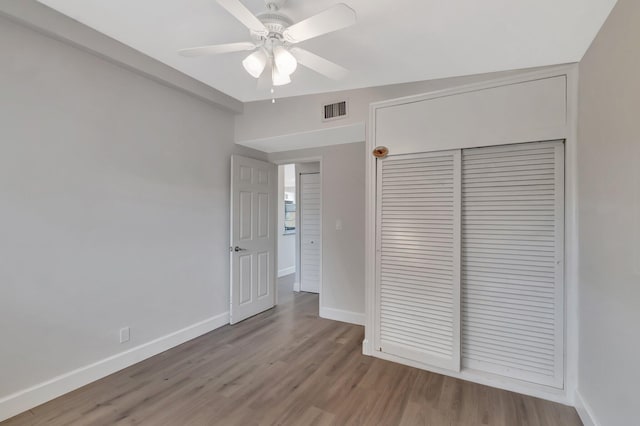 unfurnished bedroom featuring baseboards, wood finished floors, a closet, and a ceiling fan