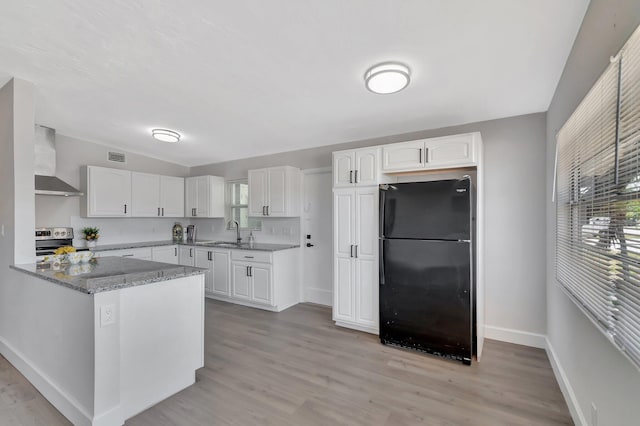 kitchen with freestanding refrigerator, stainless steel electric range oven, a sink, wall chimney range hood, and white cabinets
