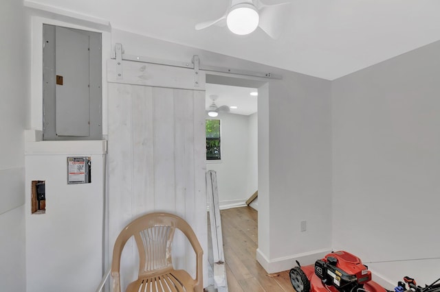 hallway with electric panel, light wood-style floors, baseboards, and a barn door