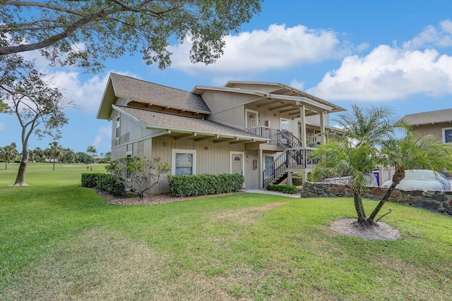 view of front of property with stairway, roof with shingles, a front yard, and covered porch