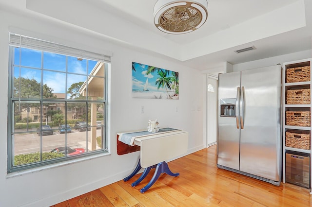 dining space with light wood-style flooring, plenty of natural light, and a raised ceiling