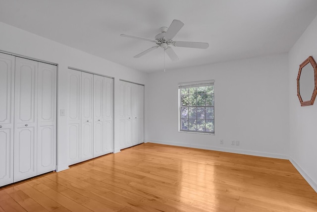 unfurnished bedroom featuring multiple closets, light wood-style floors, baseboards, and ceiling fan