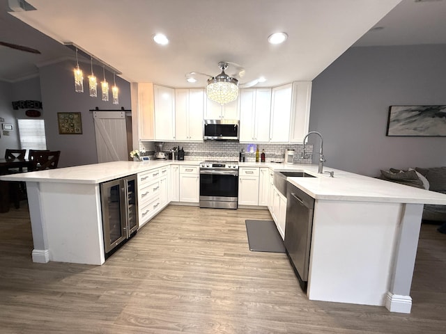 kitchen featuring appliances with stainless steel finishes, a peninsula, wine cooler, decorative backsplash, and a barn door