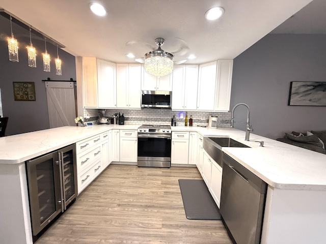kitchen featuring a peninsula, appliances with stainless steel finishes, a sink, wine cooler, and recessed lighting