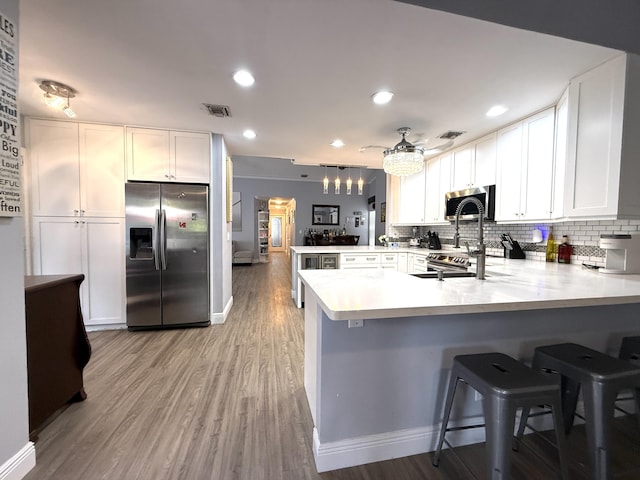 kitchen with appliances with stainless steel finishes, a peninsula, backsplash, light countertops, and white cabinetry