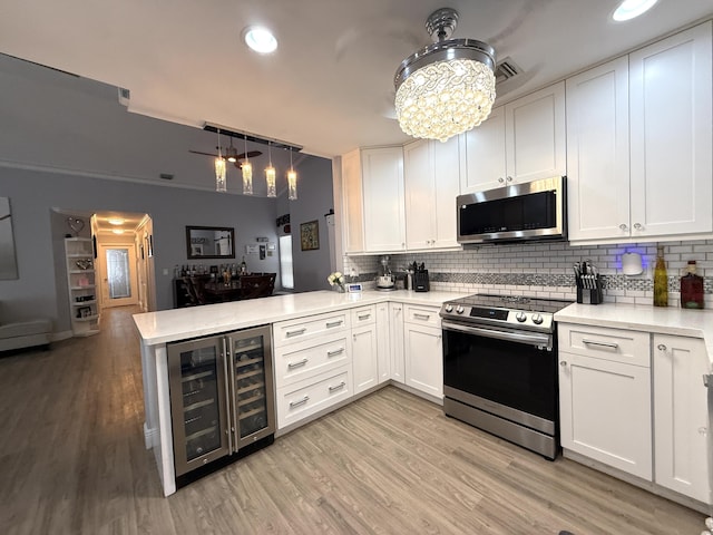 kitchen with appliances with stainless steel finishes, wine cooler, a peninsula, light countertops, and decorative backsplash