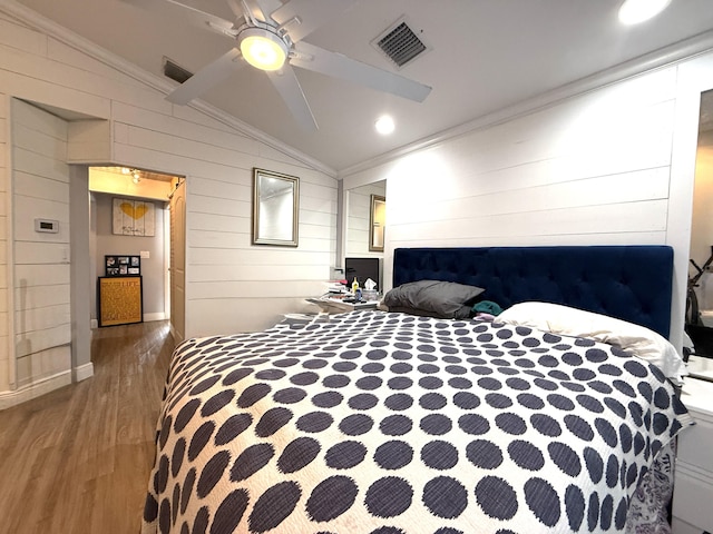 bedroom with vaulted ceiling, wooden walls, wood finished floors, crown molding, and a ceiling fan