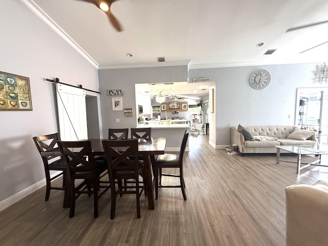dining area featuring a barn door, baseboards, ornamental molding, wood finished floors, and a ceiling fan