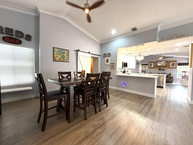 dining area with ceiling fan, ornamental molding, a barn door, lofted ceiling, and light wood-style flooring