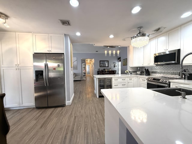 kitchen featuring stainless steel appliances, white cabinets, light wood-style floors, tasteful backsplash, and light stone countertops