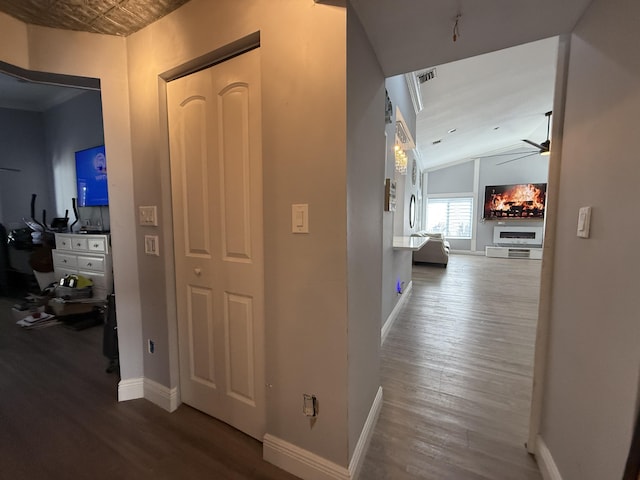 corridor featuring wood finished floors, lofted ceiling, and baseboards