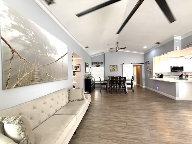 living area with a barn door, crown molding, vaulted ceiling, dark wood-style floors, and ceiling fan