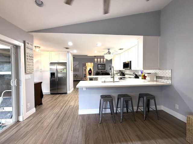 kitchen with stainless steel appliances, vaulted ceiling, a peninsula, wood finished floors, and decorative backsplash