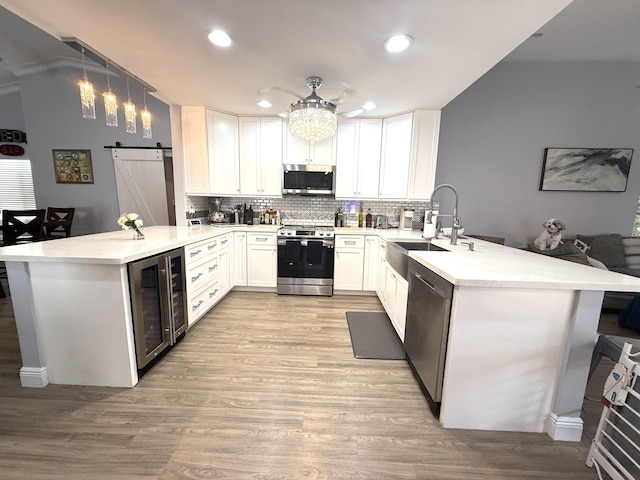 kitchen featuring appliances with stainless steel finishes, a peninsula, beverage cooler, a sink, and tasteful backsplash