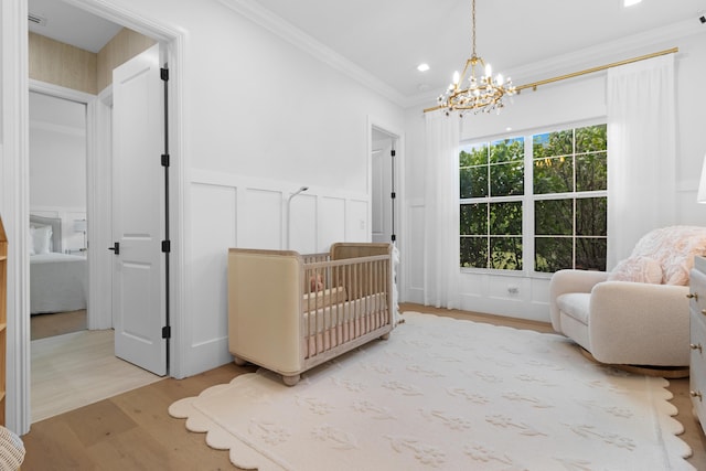 bedroom with a chandelier, light wood-style floors, ornamental molding, a decorative wall, and a wainscoted wall