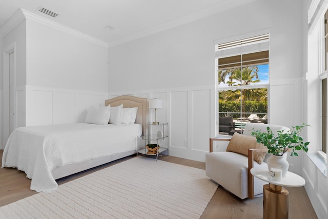 bedroom featuring a decorative wall, ornamental molding, wood finished floors, and a wainscoted wall