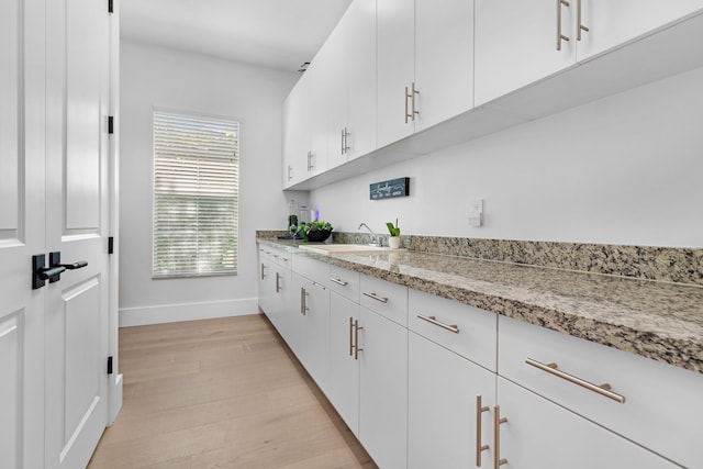 kitchen featuring a sink, baseboards, light wood finished floors, white cabinetry, and light stone countertops