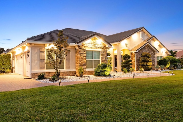 view of front of home featuring stone siding, decorative driveway, a front yard, and an attached garage