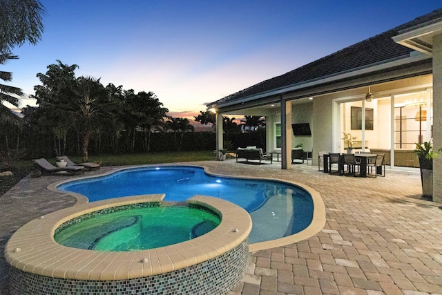 pool at dusk featuring a patio area, a pool with connected hot tub, and outdoor dining space