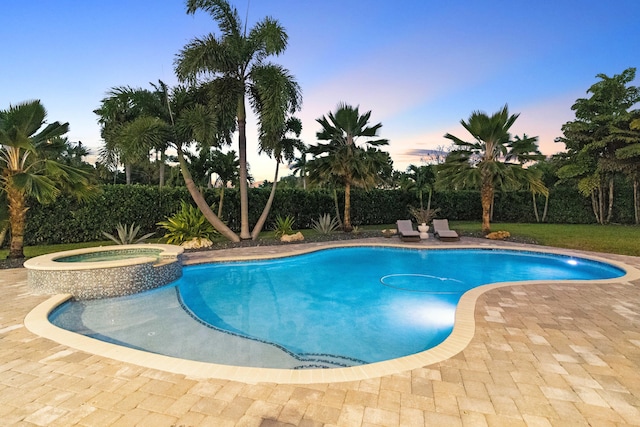 pool at dusk featuring a pool with connected hot tub and a patio