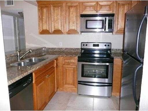 kitchen with appliances with stainless steel finishes, a sink, brown cabinetry, and dark stone countertops