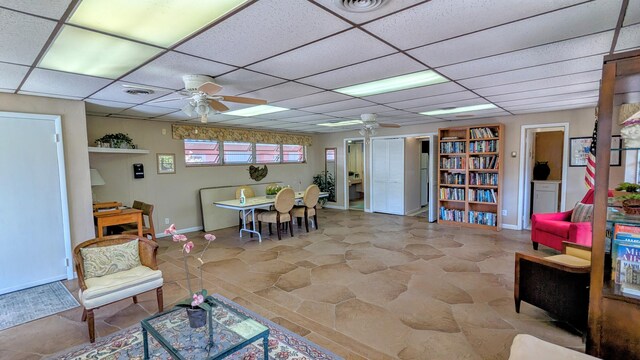 playroom with ceiling fan, a paneled ceiling, and baseboards