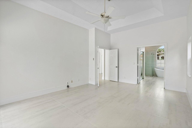 unfurnished bedroom featuring a towering ceiling, baseboards, ensuite bathroom, and a ceiling fan