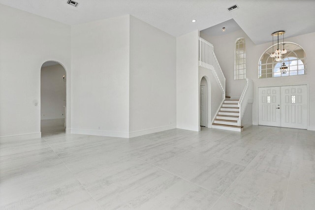 foyer entrance featuring arched walkways, a high ceiling, a chandelier, stairway, and baseboards