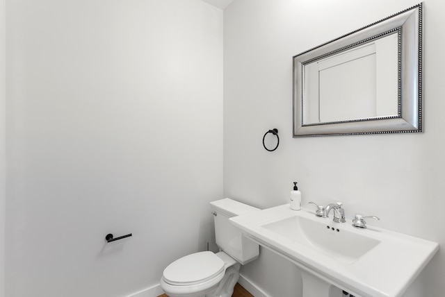 half bathroom featuring toilet, baseboards, and a sink